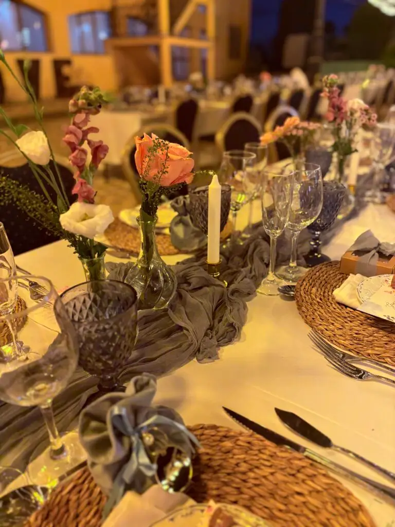 Detalle de la decoración de mesa para una boda, con bajo-platos de ratán, cristalería ahumada y centros florales, diseñada por Edesia, tu Wedding Planner en Badajoz y Córdoba.